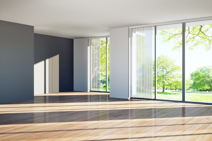 Vacant Home Insurance - Inside of a Bright Modern Vacant Home with Dark Walls and Sliding Glass Doors Leading to a Green Landscaped Yard with Trees on a Sunny Day