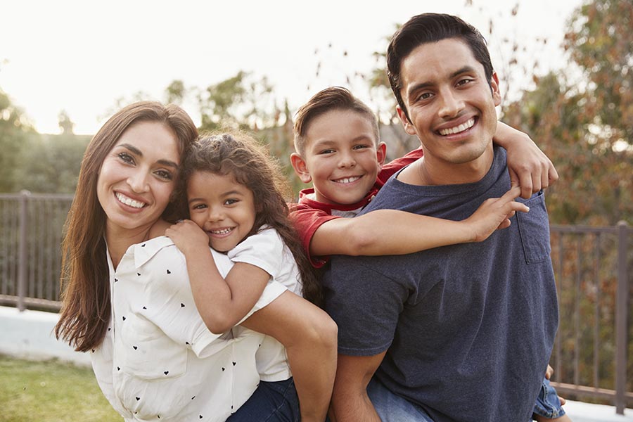 Personal Insurance - Mother, Father and Two Kids Smile in Their Yard, Kids Riding on Their Parents Backs